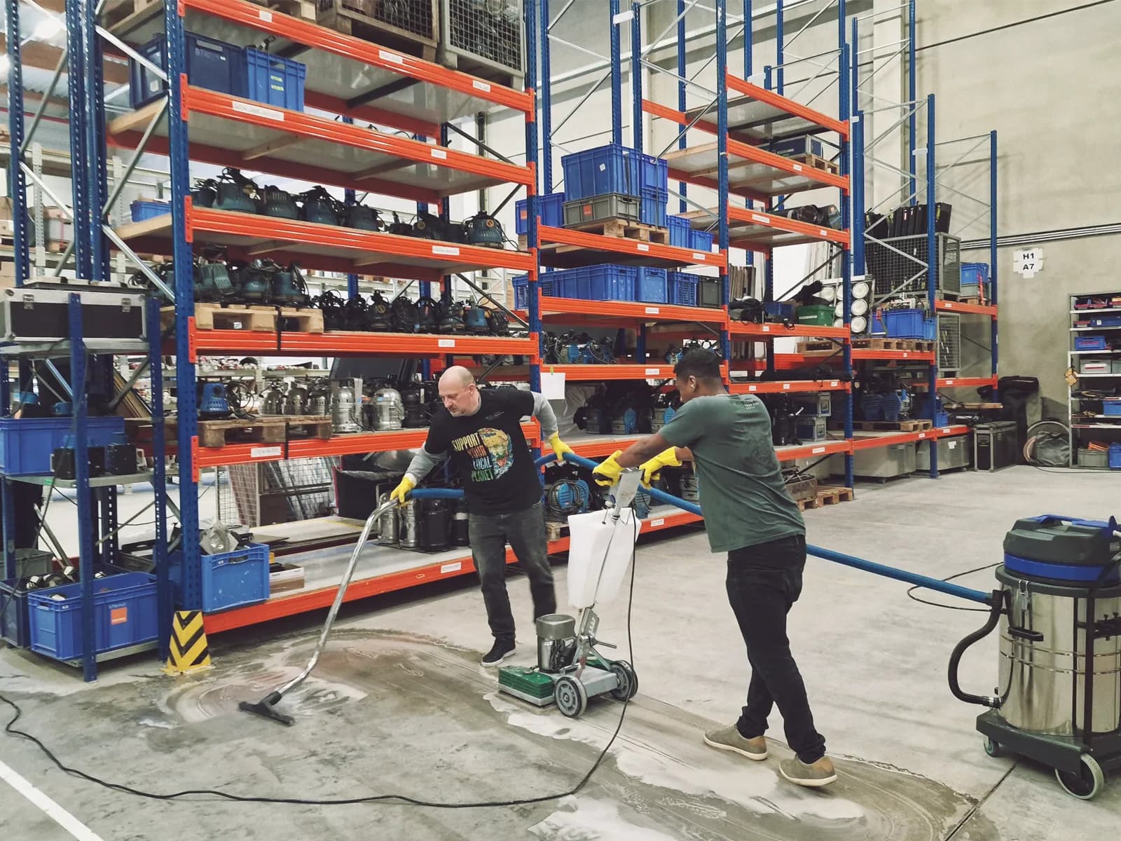 Zwei CYCG-Mitarbeiter bei der Nassreinigung einer Hallenfläche mit Einscheibenmaschine und Nasssauger