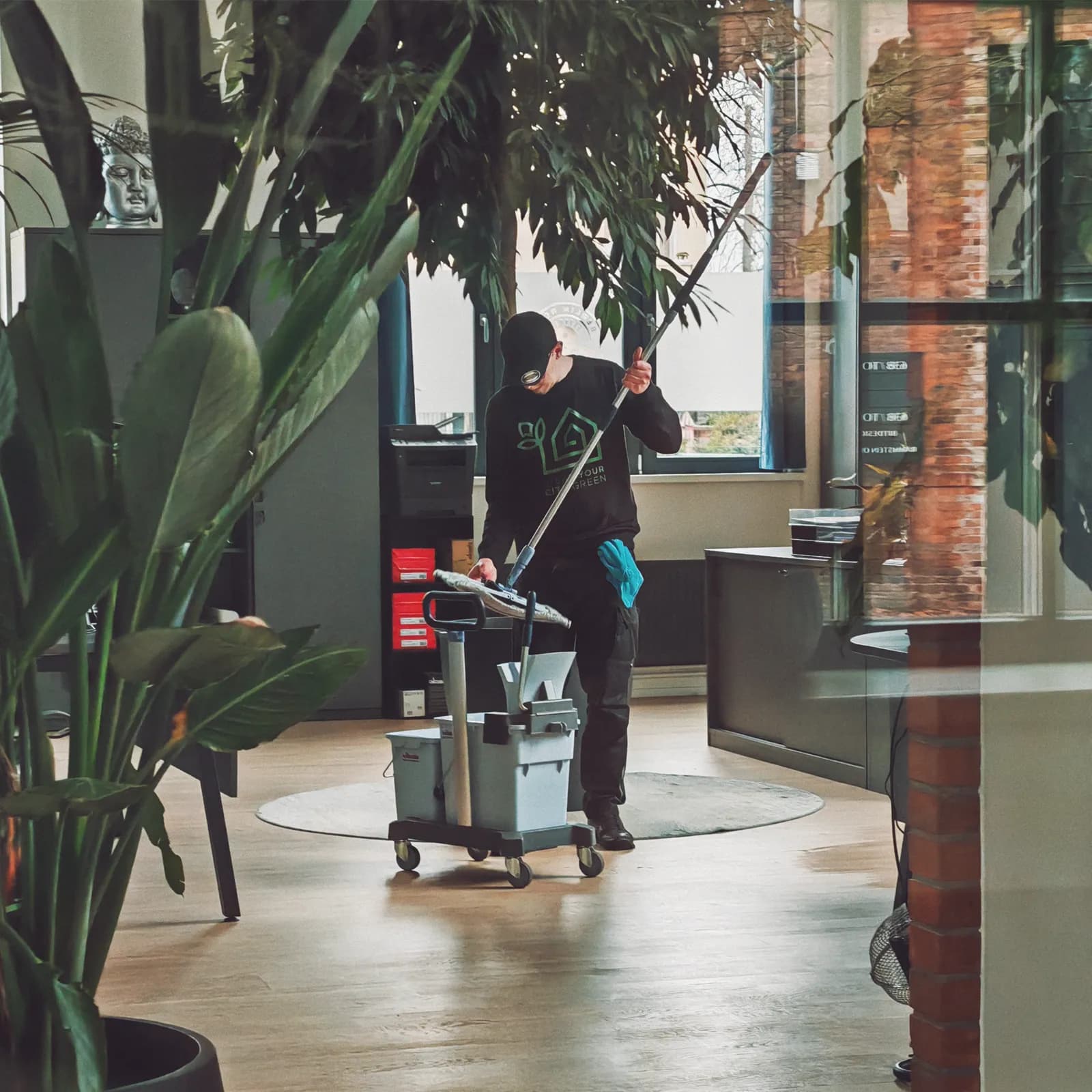 CYCG-Mitarbeiter bei der Bodenreinigung in einem Büro, aufgenommen durch eine Glaswand
