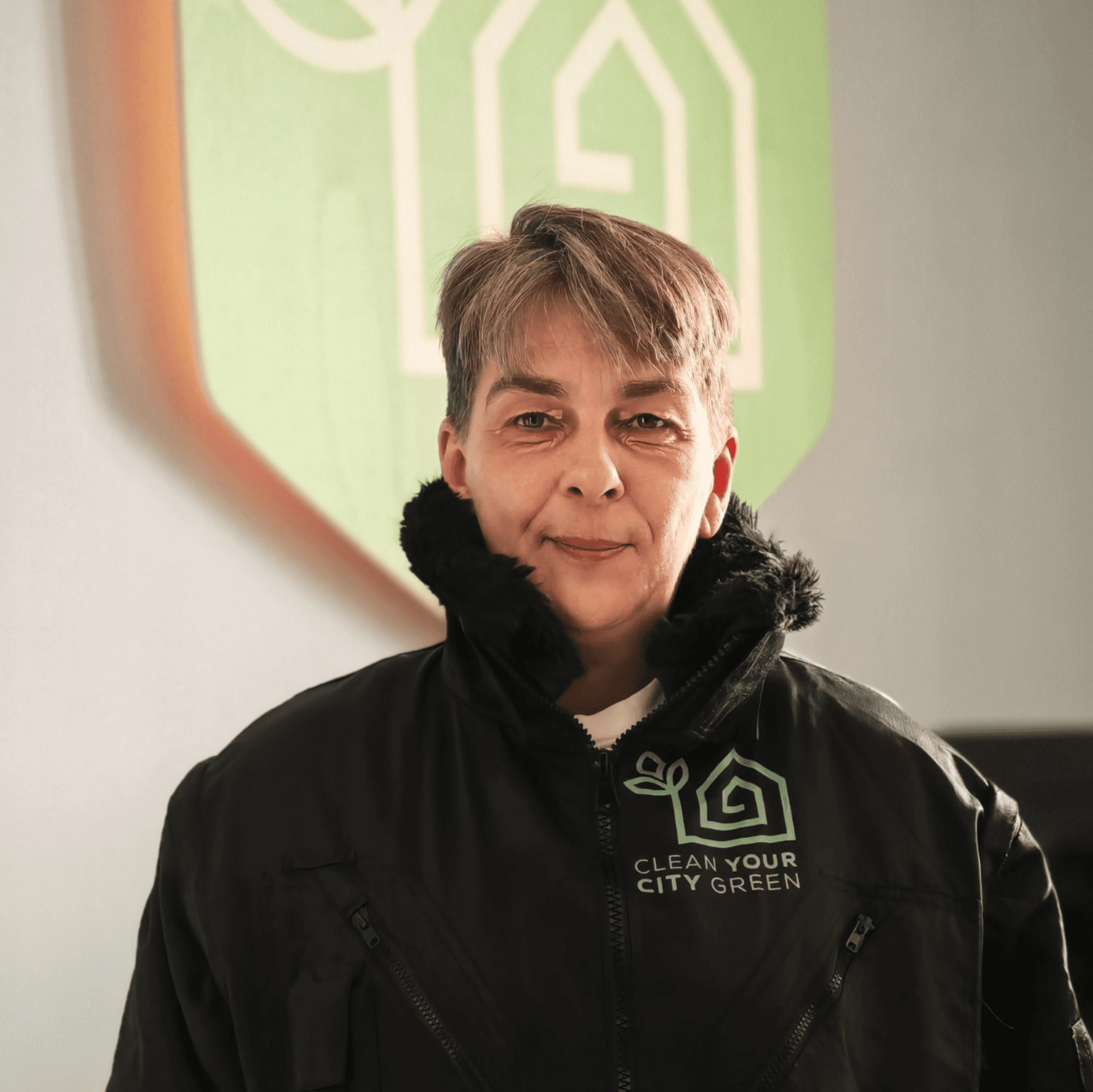 CYCG-Mitarbeiterin in Arbeitsjacke vor dem Firmenlogo